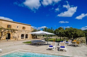 Un espace piscine avec des chaises longues, un parasol et un bâtiment doté d’arcades.
