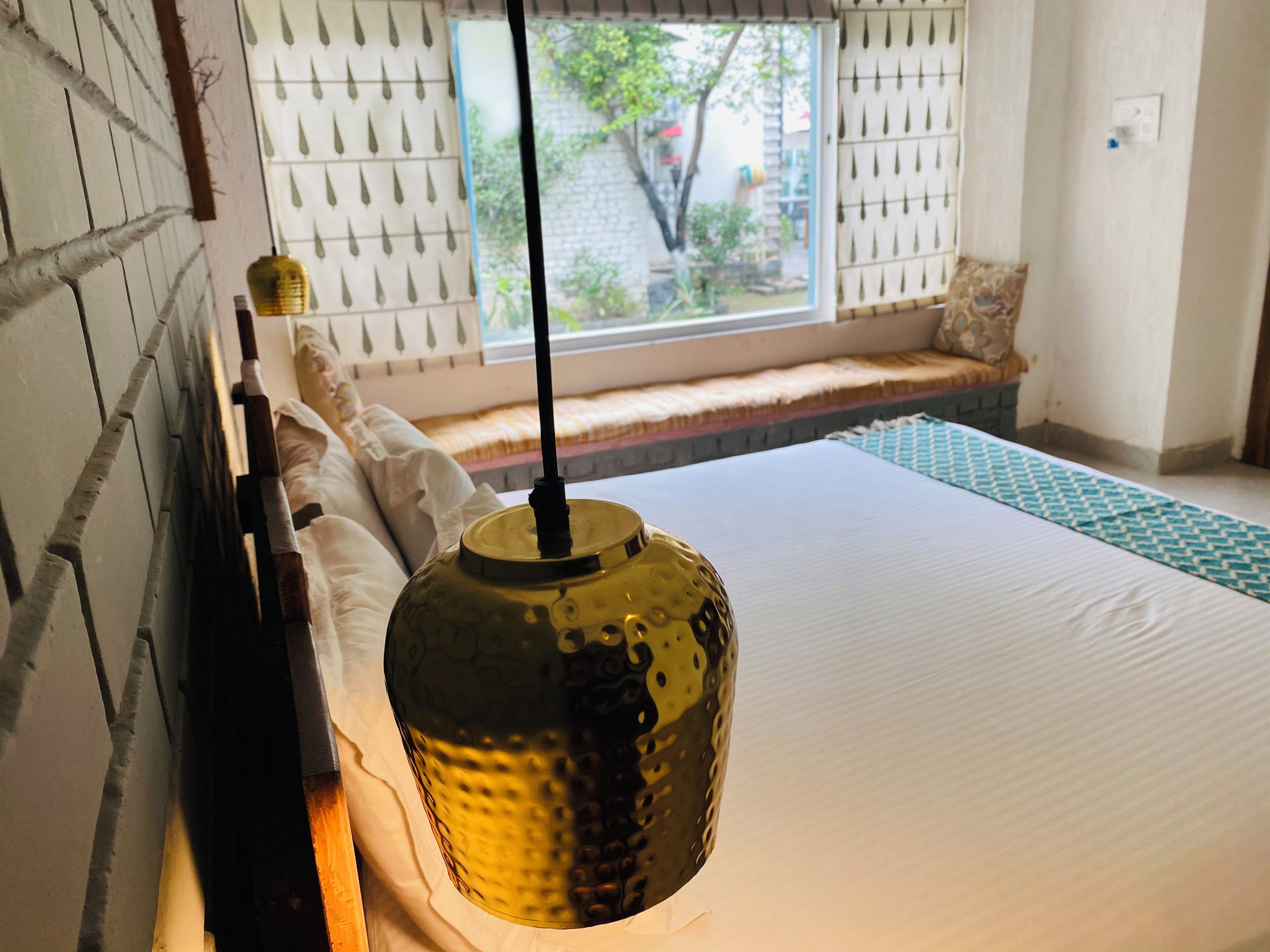 Una cama con una lámpara texturizada, una ventana con vistas a la vegetación y una alfombra estampada.
