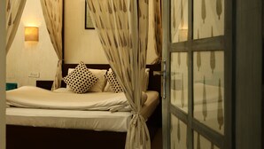 Un dormitorio con cama, cortinas, mesita de noche, lámpara de pared y una alfombra estampada.