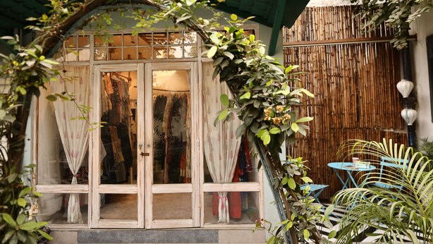Una casa tradicional con fachada de madera, cerca de bambú y una pequeña zona exterior con sillas azules.