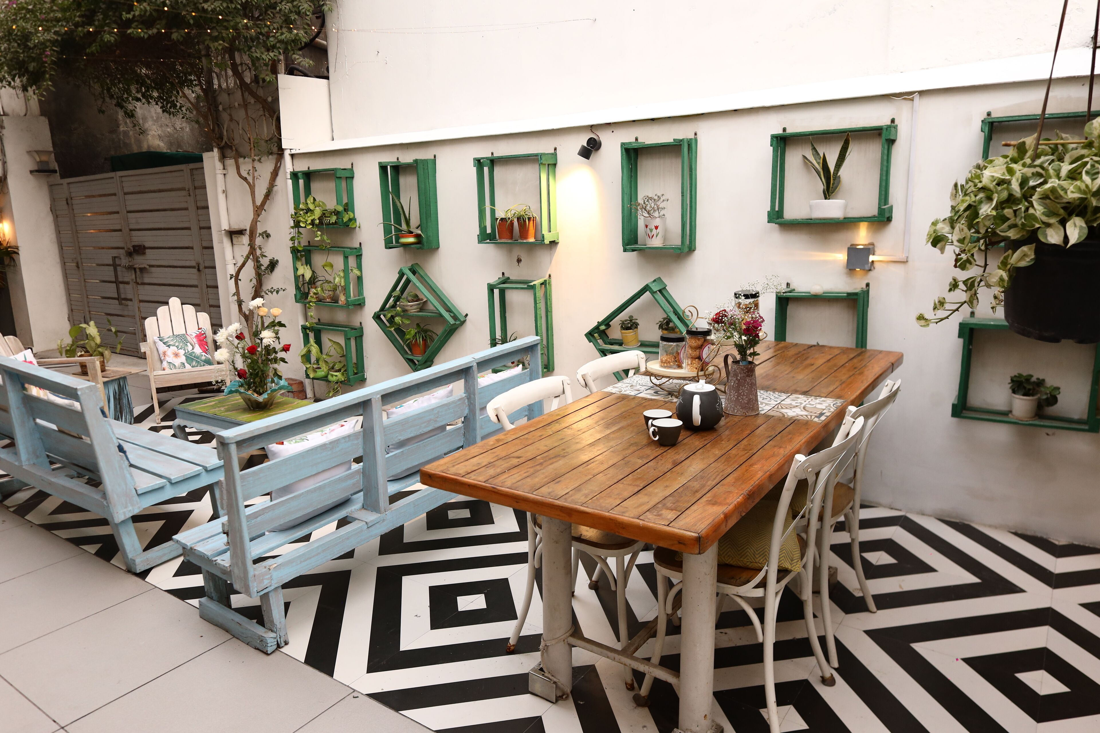 A dining area with a wooden table and chairs, surrounded by green-framed windows with plants.