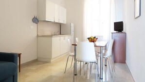 A modern kitchen with white cabinets, a dining area with white chairs, and a television on a stand. - Three-room apartment with small balcony overlooking the alleyway (Alassio)