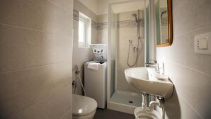 Ein kleines Badezimmer mit Toilette, Duschkabine, Waschbecken und Handtuchspender.