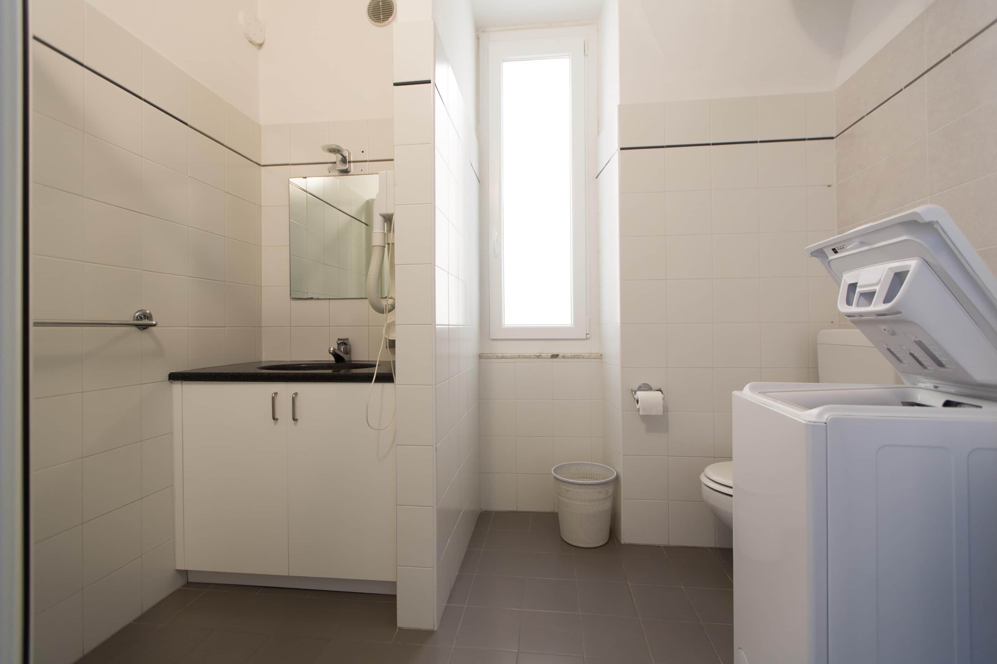 Un baño pequeño con lavamanos, espejo, ventana, inodoro y lavadora.