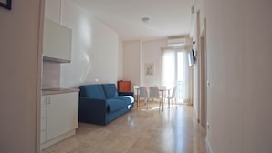 A spacious living area with a blue sofa, a dining table with chairs, and a kitchen area with cabinets. - Three-room seafront apartment with balcony (Alassio)