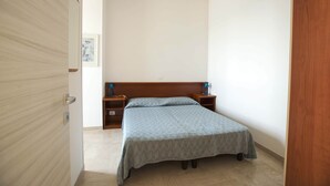 A bedroom with a bed, wooden headboard, bedside tables, and a nightstand. - Three-room seafront apartment with balcony (Alassio)