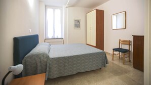 Un dormitori amb llit, escriptori, cadira, armari i finestra.