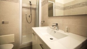 Un bany modern amb dutxa trencada per vidre, un lavabo blanc i un mirall gran.