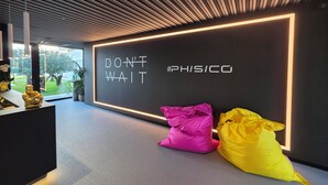 Un intérieur moderne agrémenté d’un mur d’inspiration sur lequel on peut lire : « N’attendez pas, passez à l’action ! #PHISICO », et offrant une vue sur un jardin.