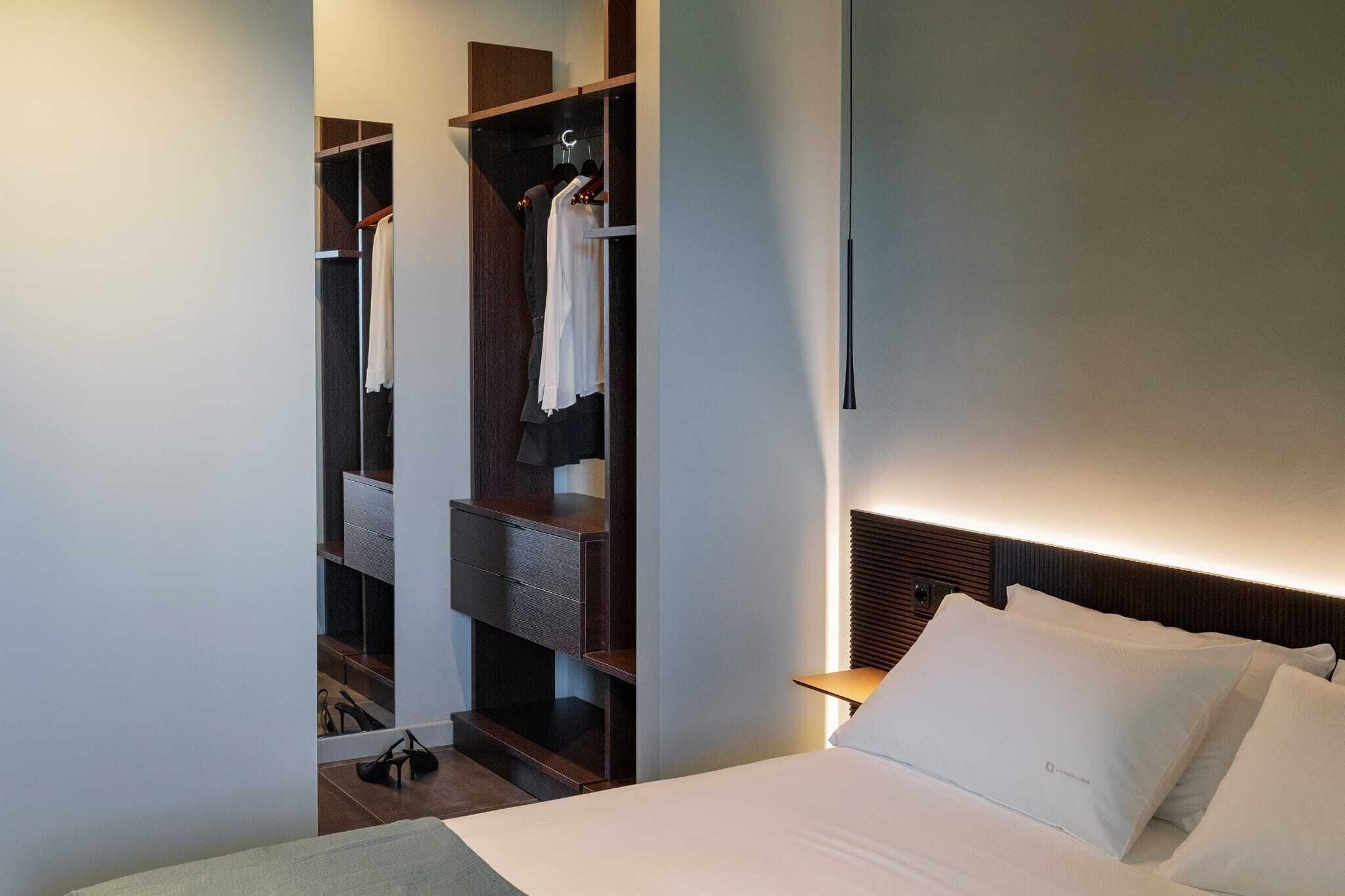 A modern hotel room with a bed, a built-in wardrobe, and a bedside table.
