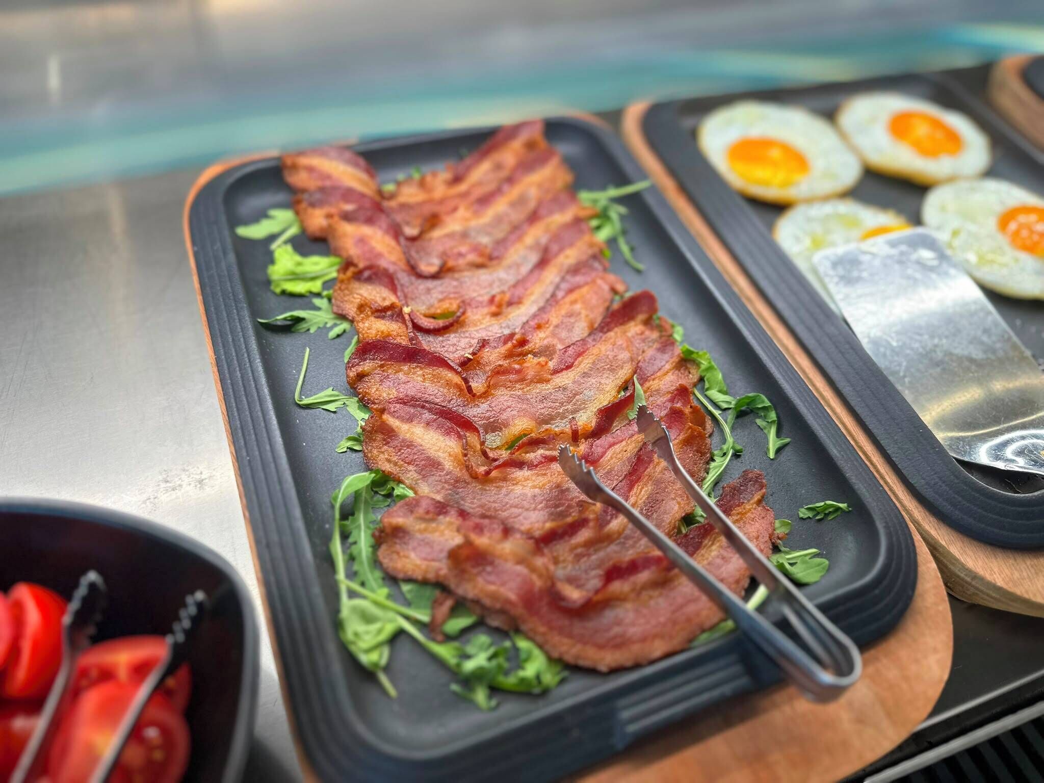 En morgenmadsanretning med bacon, grønt og æg på et fad.