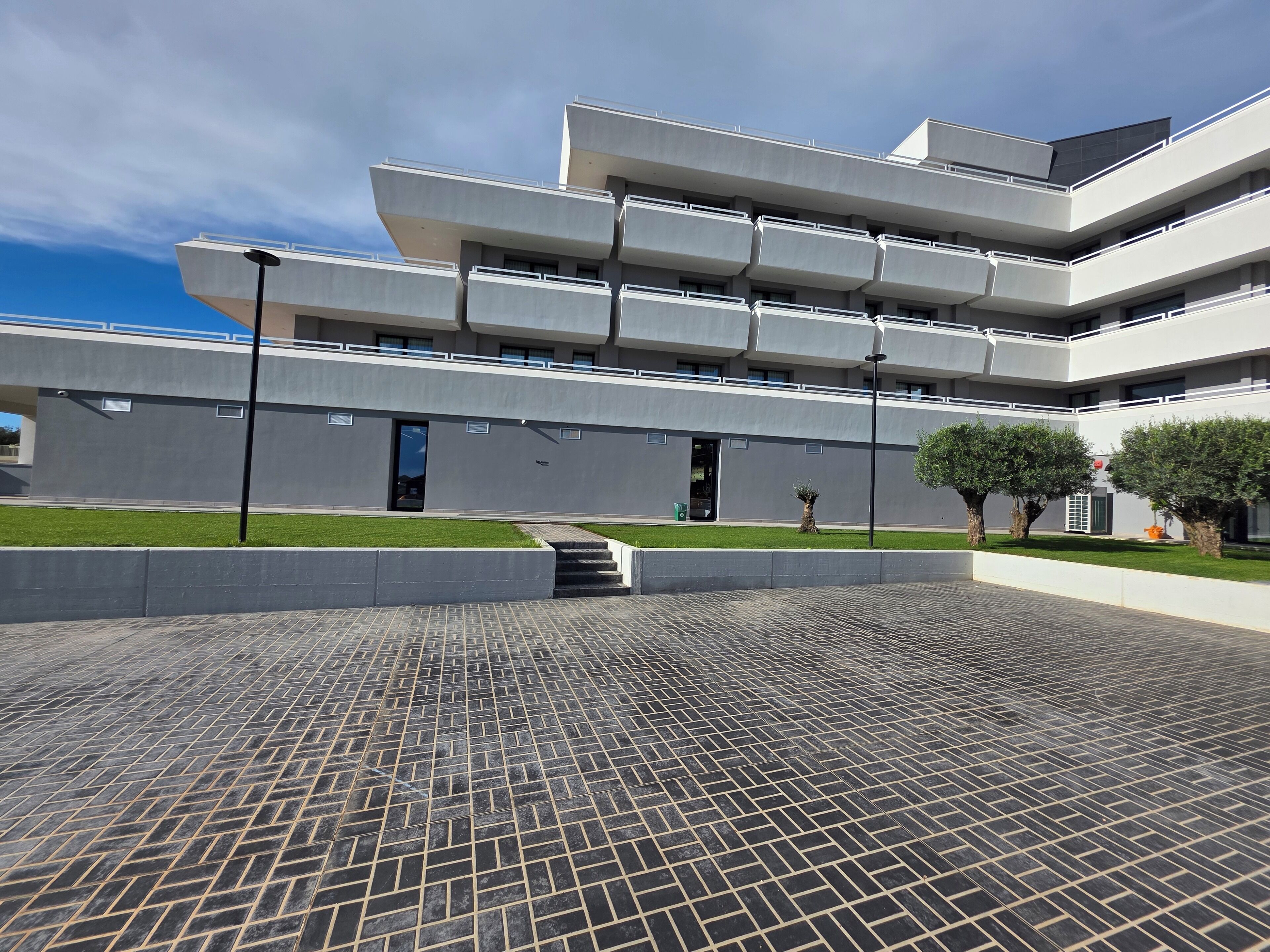 A modern building with a flat roof, multiple balconies, and a paved courtyard.