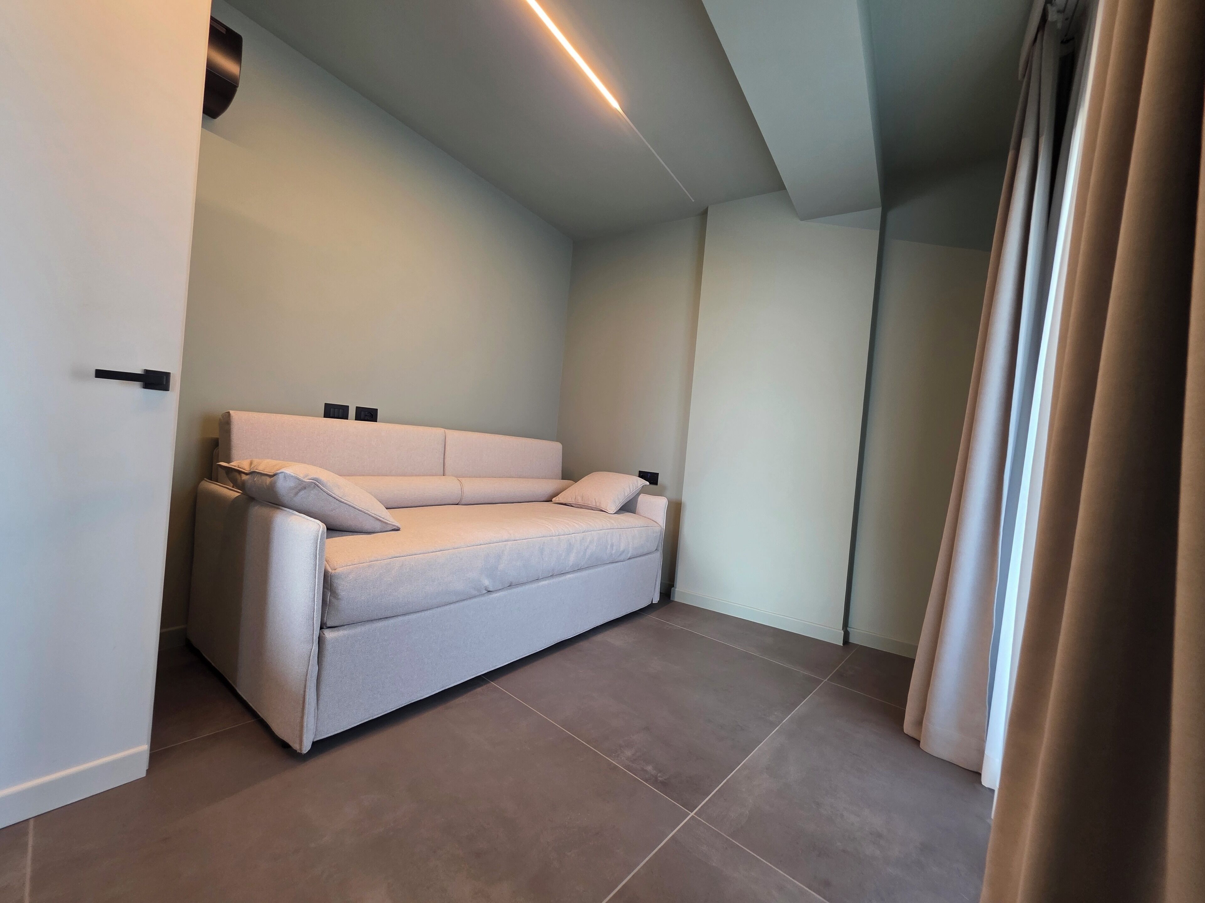 A modern, minimalist room with a beige sofa, a ceiling light, and a window with curtains.