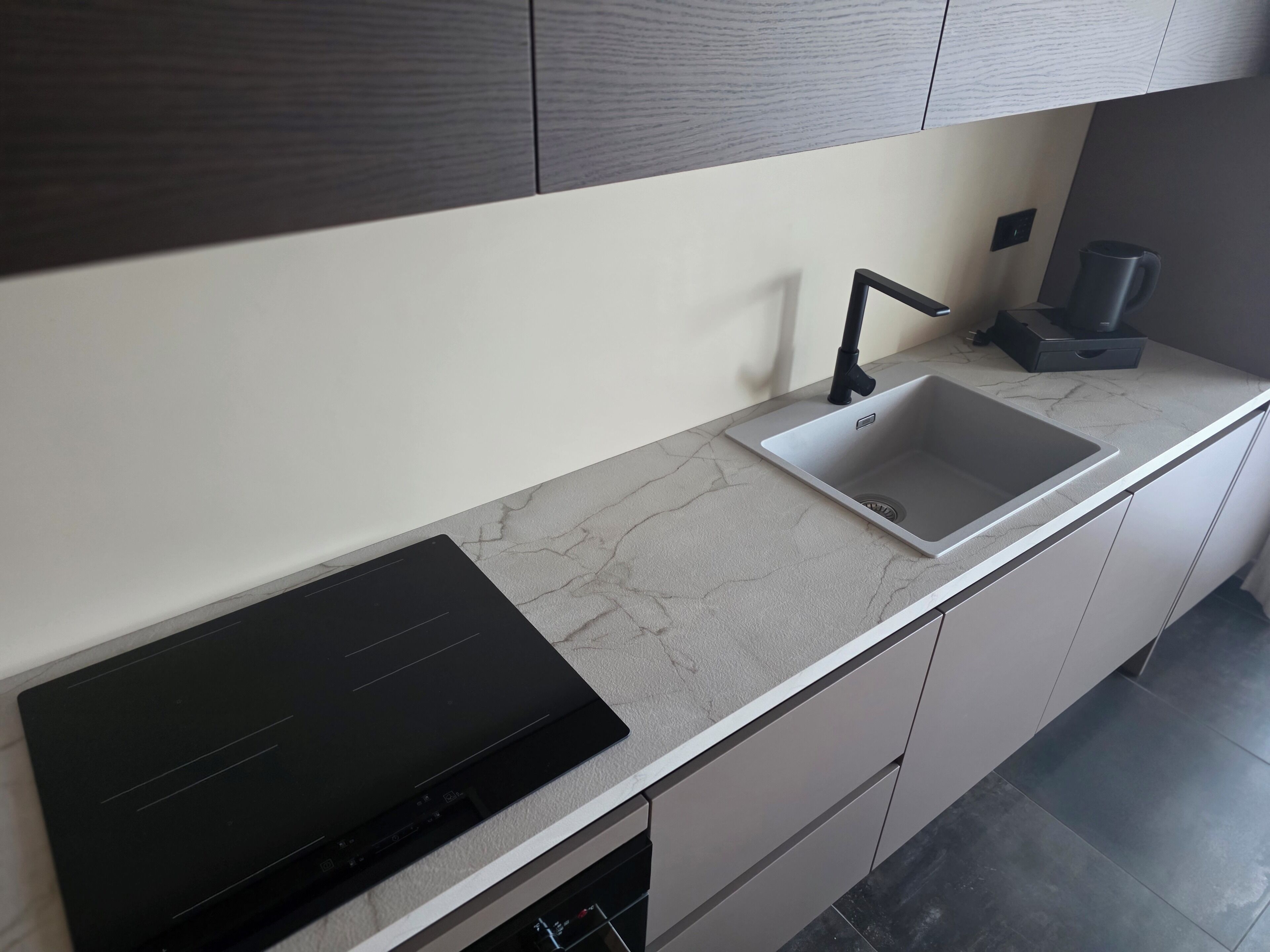 Una cocina moderna con una placa de inducción integrada, un lavamanos de acero inoxidable y armarios grises.