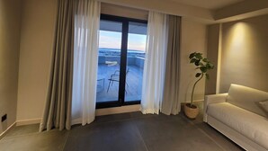 Un salon moderne doté d’une grande porte-fenêtre coulissante donnant sur un balcon. La pièce est agrémentée d’un canapé beige, d’une plante en pot et offre une vue sur le paysage urbain.