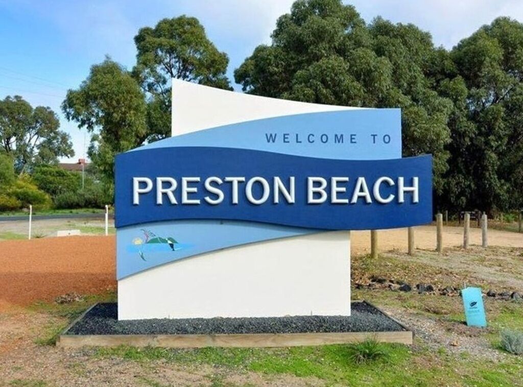 A welcome sign for Preston Beach with a clear sky and trees in the background.