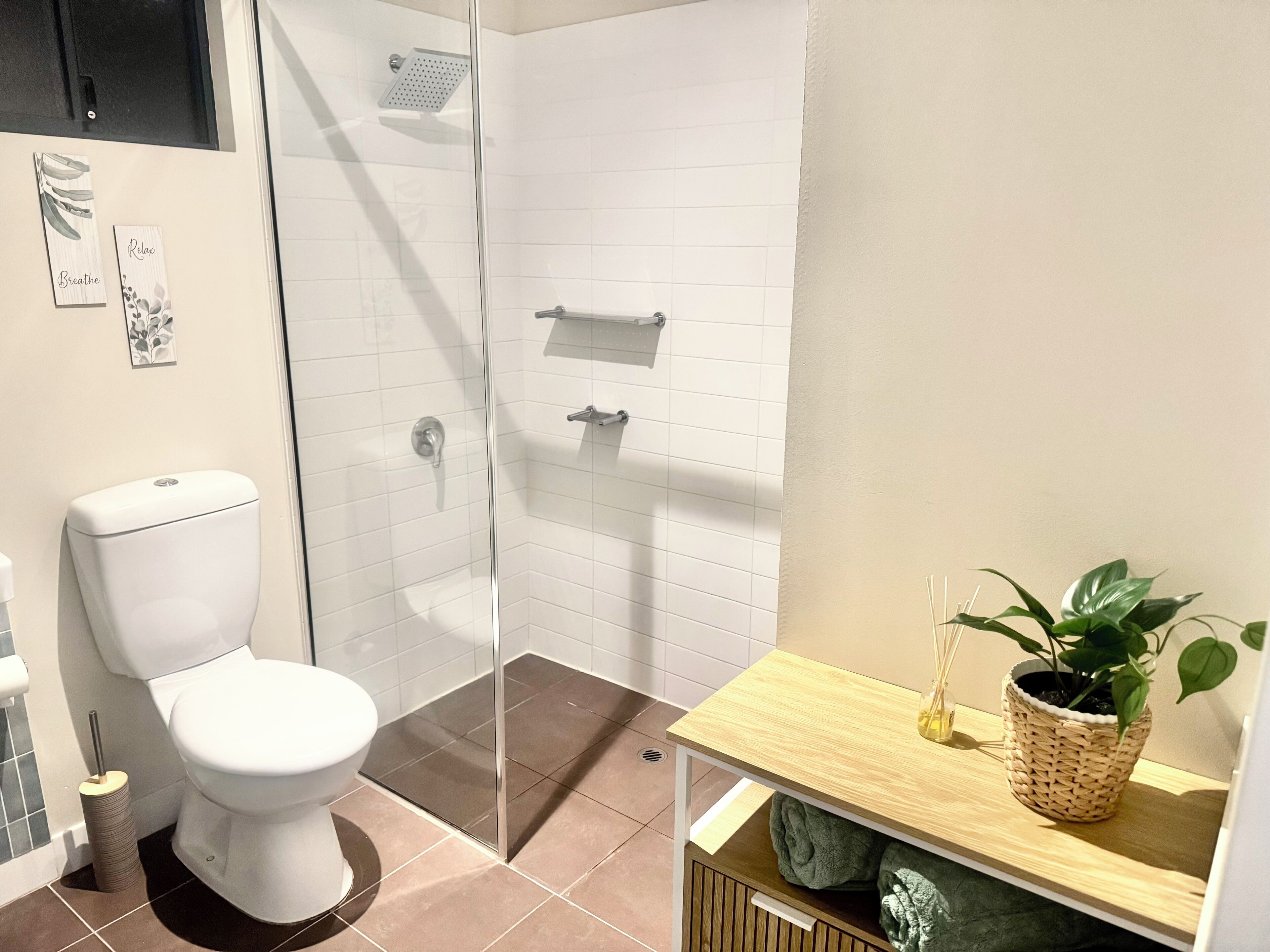 Une salle de bain comprenant des toilettes, un espace de douche vitré, un lavabo avec un plan de travail en bois et une plante en pot.