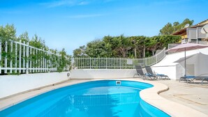 A swimming pool with a white fence, lounge chairs, and a building in the background. - Miramar Apartment with sea views (Alcúdia)