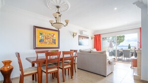 A modern living room with a dining area, a sofa, and a view of the sea. - Miramar Apartment with sea views (Alcúdia)