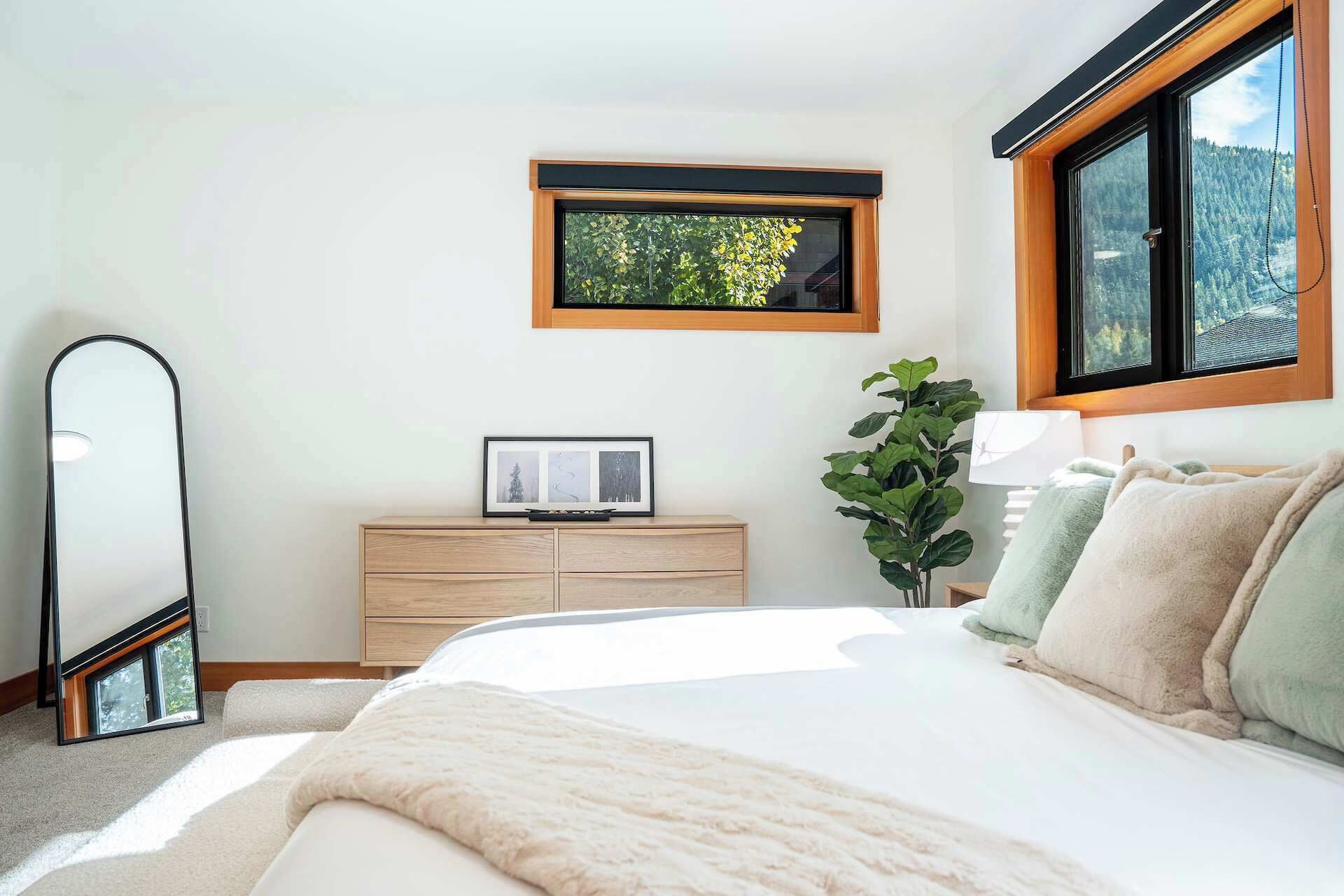 Een slaapkamer met een bed, een kaptafel, een spiegel, een raam en een plant.