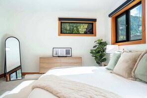 Un dormitorio con cama, cómoda, espejo, ventana y planta.
