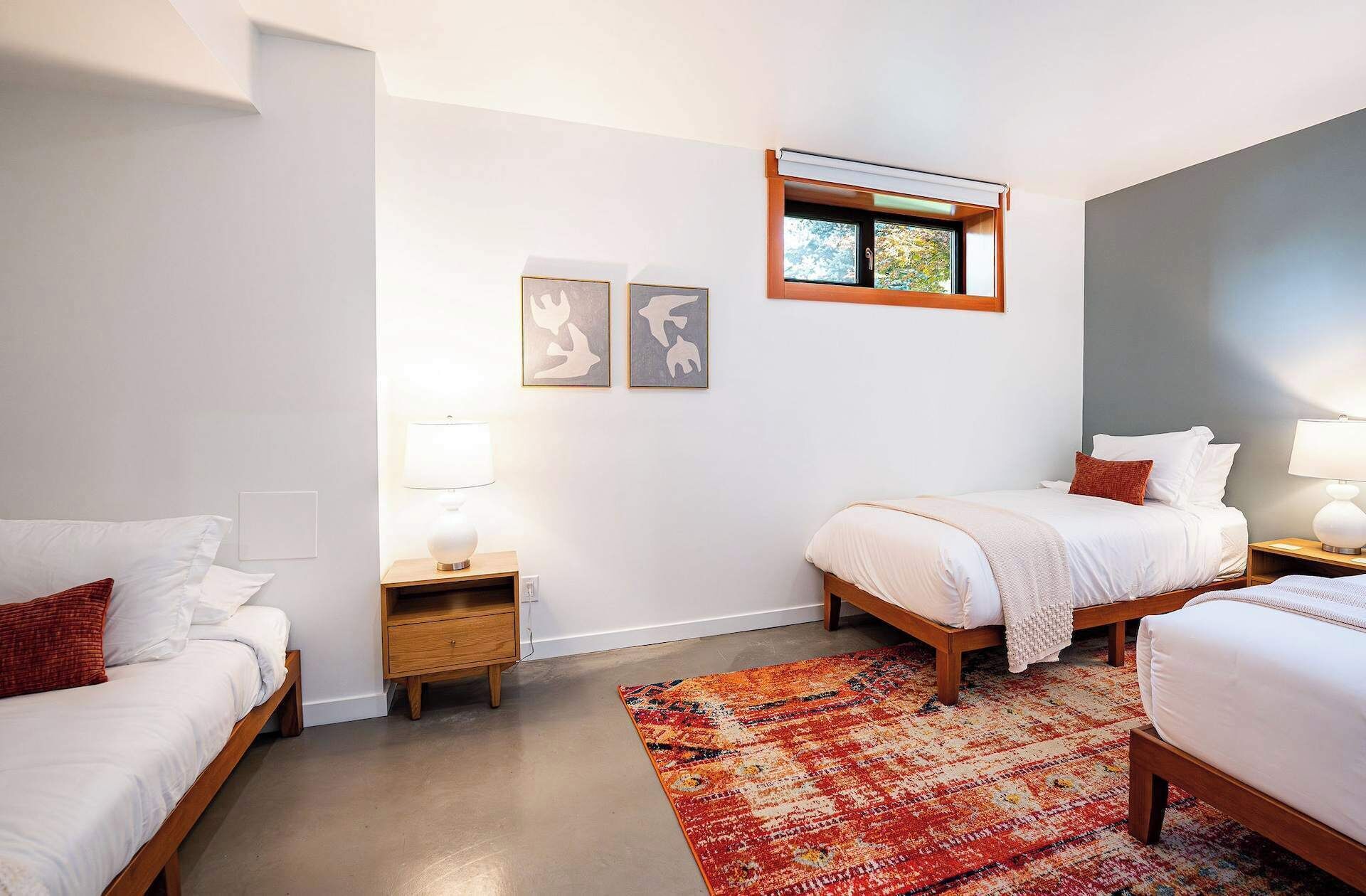 A hotel room with two beds, a small window, a rug, and two wall art pieces.