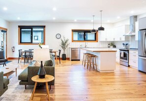 A modern kitchen with a central island, wooden flooring, and a dining area with a sofa and table.