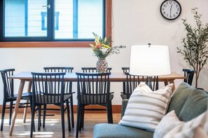 Un comedor con una mesa de madera, sillas negras, un florero con flores, un reloj de pared y una lámpara.