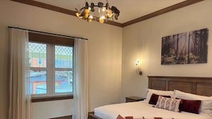 Ein Schlafzimmer mit einem großen Bett, einer Bank, einem Kronleuchter, einem Gemälde und einem Fenster mit Vorhängen.