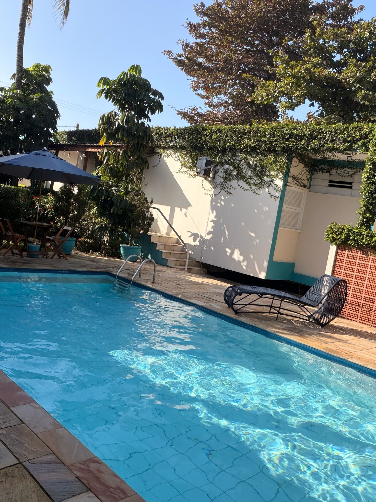 Une piscine avec une terrasse carrelée, un fauteuil de relaxation et un escalier menant à un bâtiment.