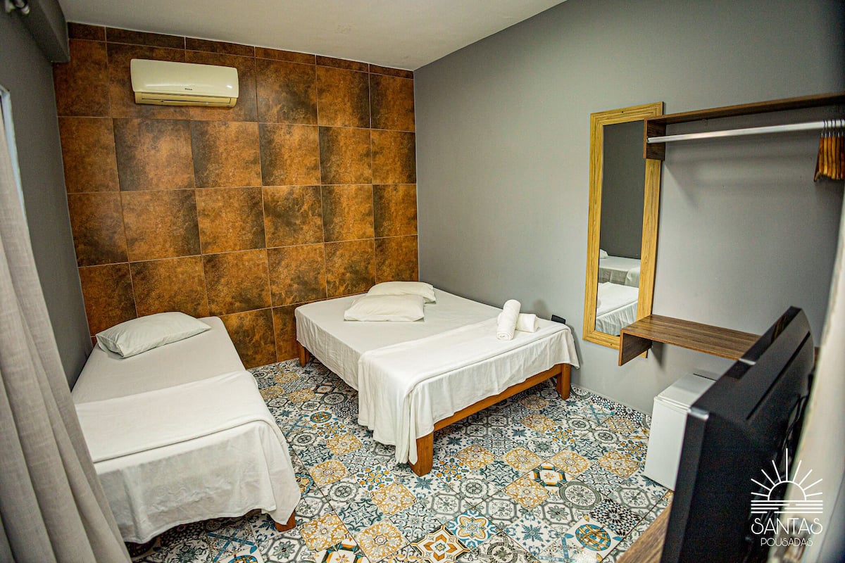 A small, clean room with two beds, a mirror, and a TV.