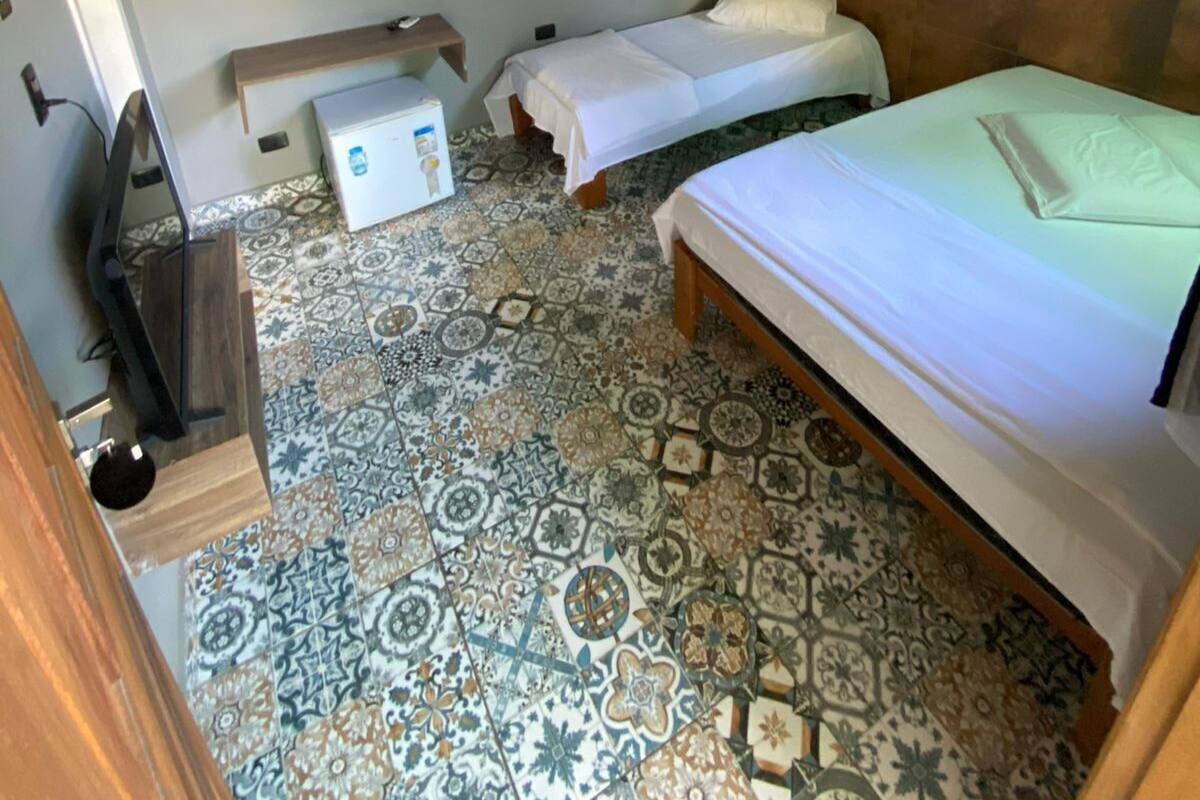 A room with two beds, a small table, a TV, and a wall-mounted shelf with towels.