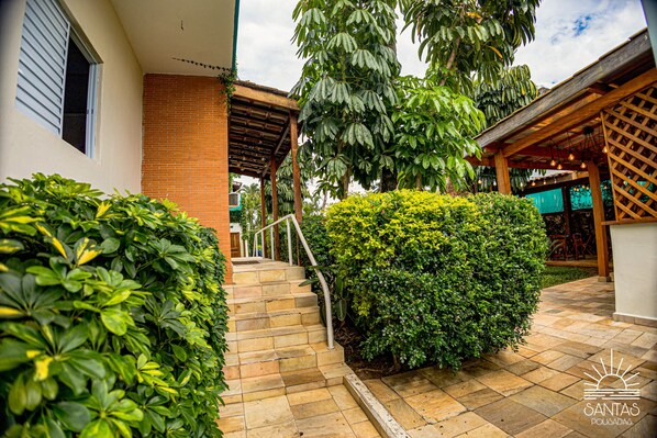 A courtyard with a brick wall, a wooden pergola, and a staircase leading to a covered area.