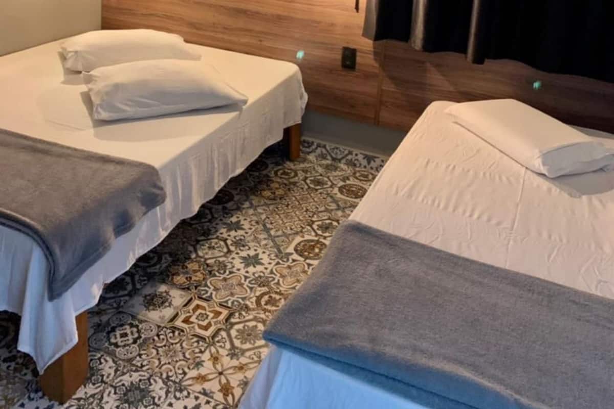 A hotel room with two beds, a wooden headboard, a wall-mounted air conditioner, and a painting of a cityscape.