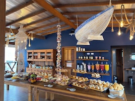 A breakfast buffet with various pastries and fruits, wooden furniture, and a blue wall with shelves of condiments.