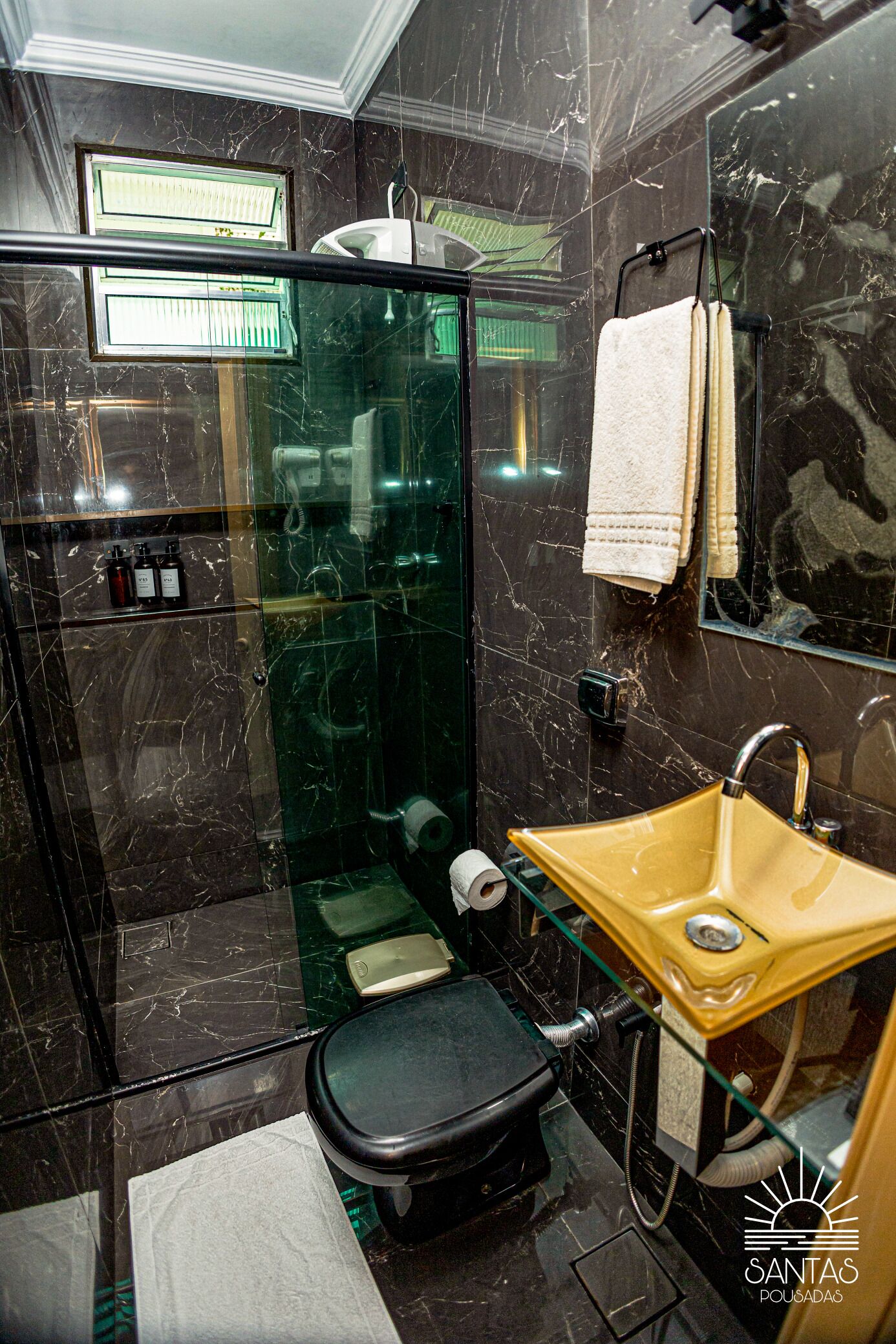 Um banheiro moderno com chuveiro em cabine de vidro, vaso sanitário preto, pia amarela e paredes de mármore.