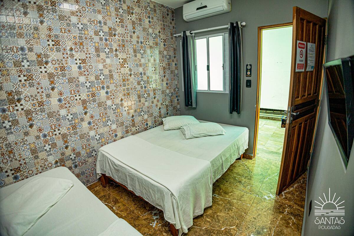 A room with two beds, patterned walls, a window with curtains, and a door.