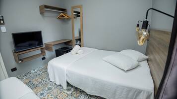 Hotellihuone, jossa on sänky, televisio, peili, riippuvalaisin ja kuviollinen lattia.