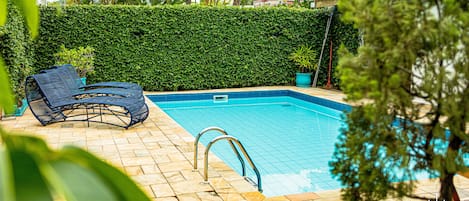 A swimming pool with a tiled edge, a metal ladder, and a blue lounge chair.