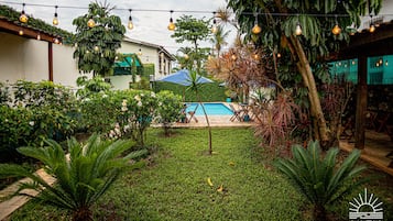 A backyard with a swimming pool, surrounded by lush greenery and string lights.