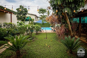 A backyard with a swimming pool, surrounded by lush greenery and string lights. - Santa Cecília Pousada (Guarujá)