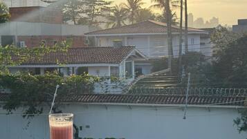 A balcony with a glass of beverage and a plate of fruit, overlooking a residential area with buildings and palm trees.
