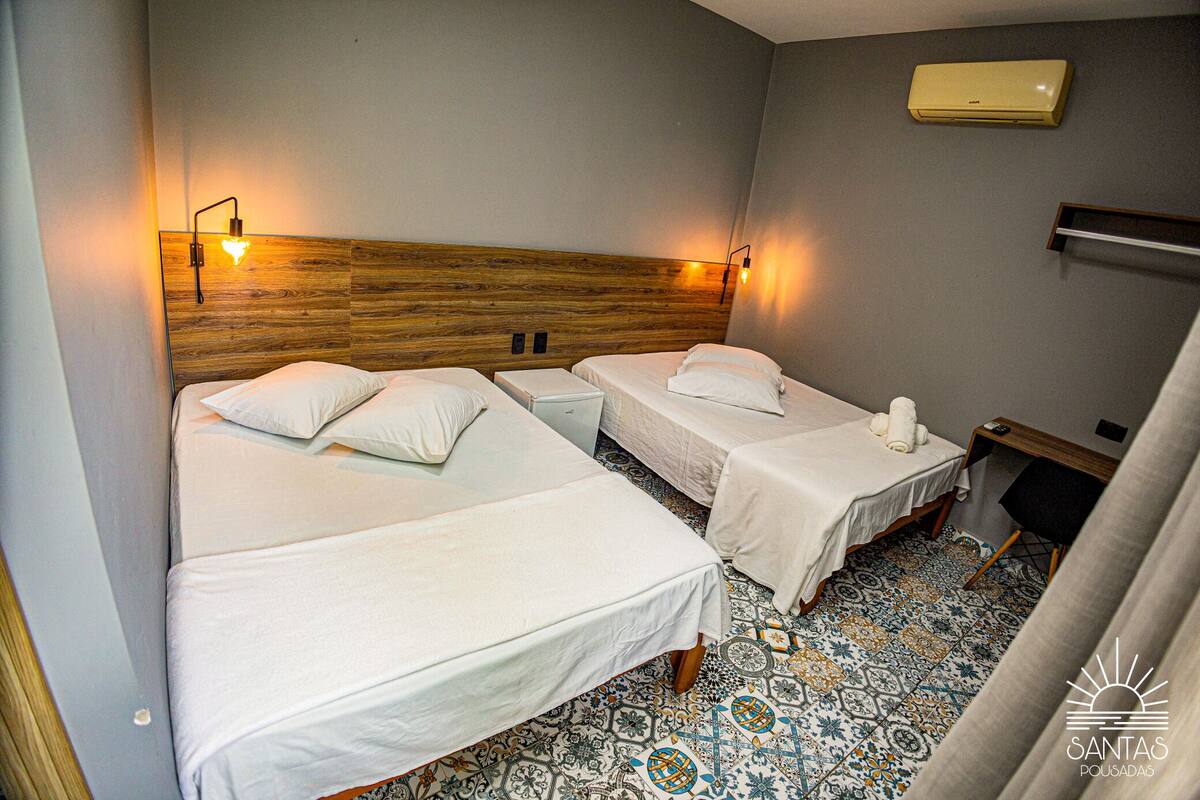 A hotel room with two beds, a wooden headboard, a tiled floor, and a wall-mounted air conditioner.
