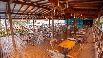 An outdoor dining area with wooden tables and chairs, a covered roof, and hanging light fixtures.