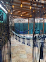 A hammock suspended between macramé ropes, a wooden ceiling, and a tiled floor.