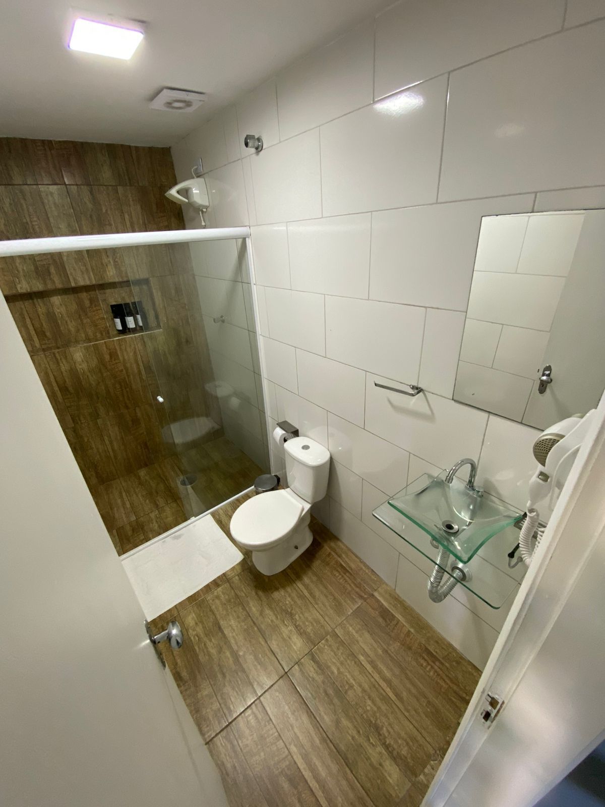 Un baño pequeño con lavabo de vidrio, inodoro y zona de ducha.