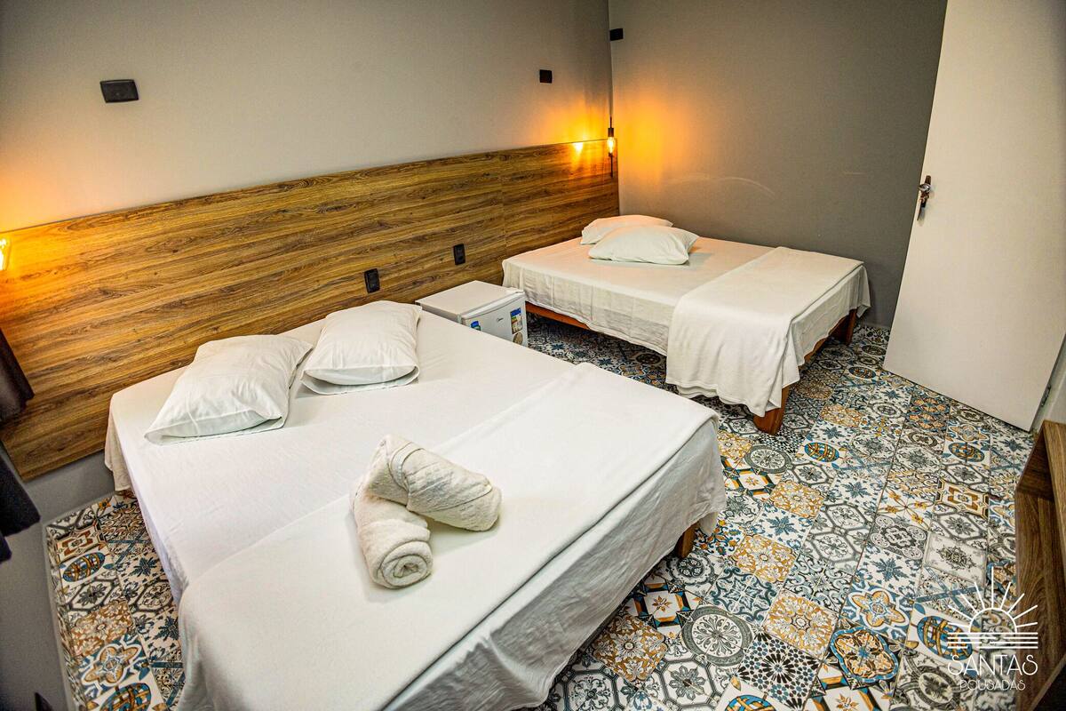 A hotel room with two beds, a wooden headboard, patterned floor tiles, and a small white cabinet.