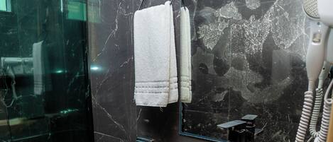 Casa de banho moderna com chuveiro em cabine de vidro, sanita preta, lavatório de vidro e secador de cabelo.