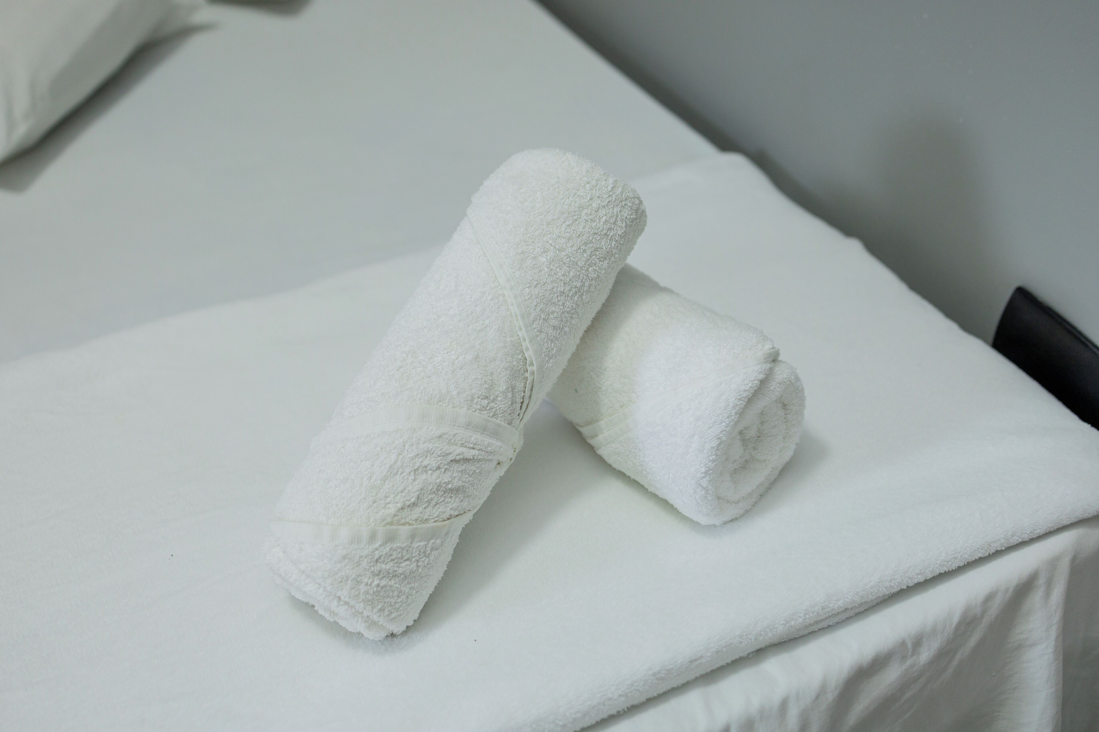 A neatly made bed with white linens and two rolled towels placed on top.