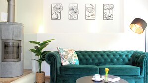 Una sala de estar con sofá verde, una mesa de centro, planta en maceta, chimenea y cuadros en la pared.